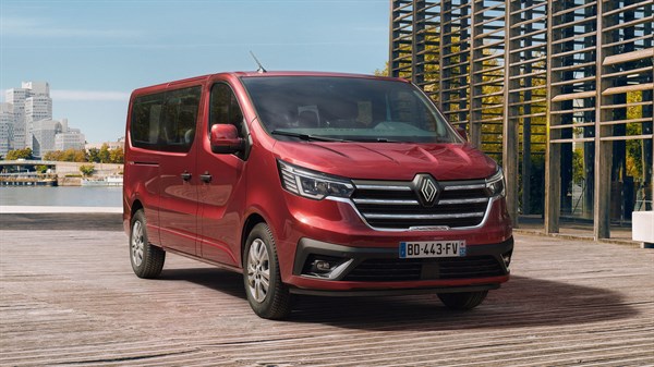 Renault Trafic Passenger v elegantni rdeči barvi, parkiran ob vodi v urbanem okolju – sodoben in prostoren kombi za prevoz več potnikov.