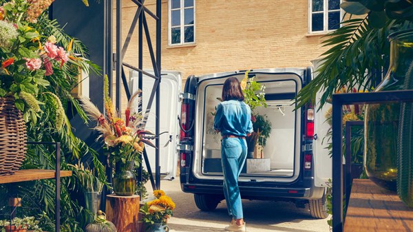 Renault Trafic Van parkiran pred cvetličarno, oseba nalaga rastline v zadnji del vozila.