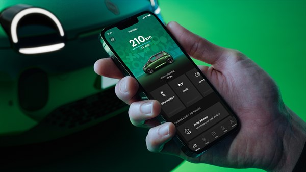 Roka drži pametni telefon z aplikacijo za daljinsko upravljanje Renault vozila Twingo, v ozadju je sprednji del vozila.