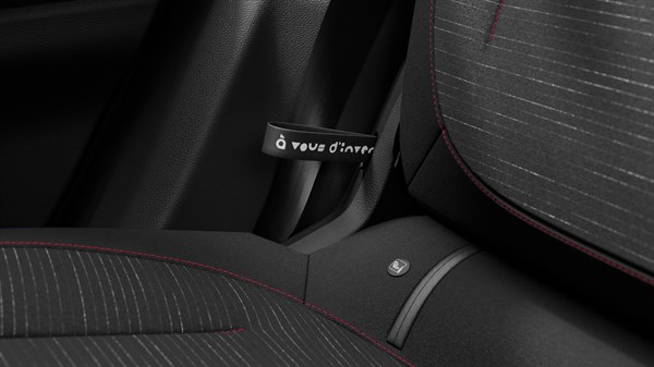 Detajl notranjosti vozila, pogled na trak za nastavitev zadnjega sedeža z napisom ob sedežnem oblazinjenju.