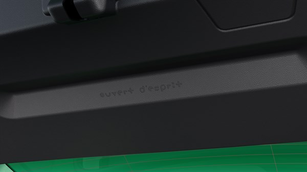 Detajl notranjosti vozila, bližnji pogled na napis "ouvert d'esprit" na notranji oblogi prtljažnih vrat.