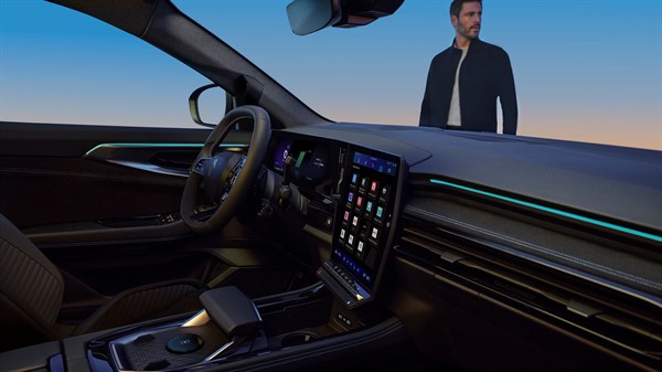 Notranjost vozila Renault s poudarkom na volanu in osrednjem zaslonu na dotik, zunaj avtomobila stoji moški.