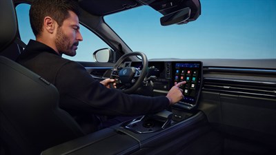 Moški za volanom vozila Renault Austral se dotika osrednjega zaslona na dotik.