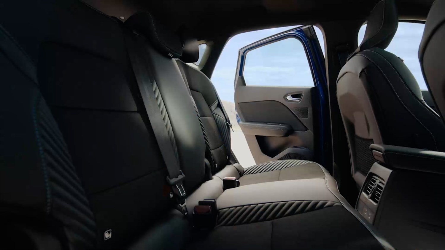 Zadnji sedeži vozila, pogled s strani skozi odprta zadnja vrata, vidna sta črna oblazinjenja z modrimi šivi.