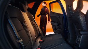 Zadnji sedeži vozila, pogled s strani skozi odprta zadnja vrata, vidna sta črna oblazinjenja z modrimi šivi.