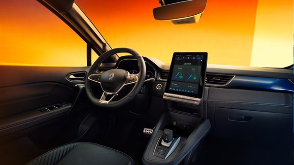 Notranjost vozila z volanom in pokončnim sredinskim zaslonom na dotik, osvetljena z oranžno svetlobo v ozadju.