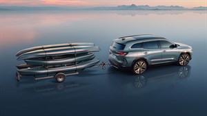 Modro-sivi Espace z nameščeno vlečno kljuko vleče prikolico z naloženimi štirimi kajaki, parkiran na zrcalni površini z ozadjem sončnega zahoda.