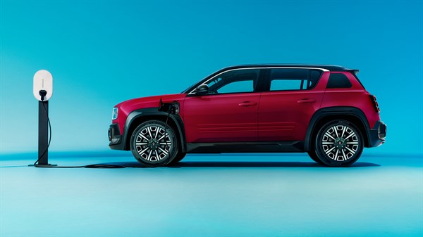 Profil rdečega Renault 4 E-Tech Electric, priključen na polnilno postajo na levi strani, na svetlo modrem ozadju.