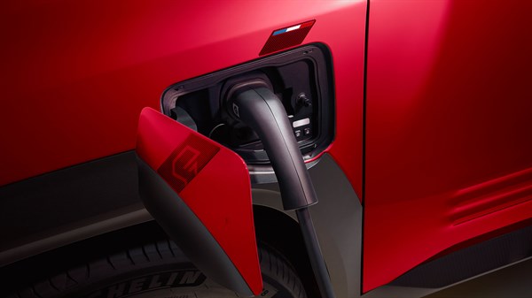 Odprt pokrov polnilnega vtiča na levi sprednji strani Renault 4 E-Tech Electric z vstavljenim polnilnim kablom.