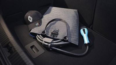 Polnilni kabel za električno vozilo Renault, shranjen v elegantni torbi z ročaji, poleg katere je postavljena črna kapa z logotipom Renault, vse skupaj položeno v prtljažnik vozila.