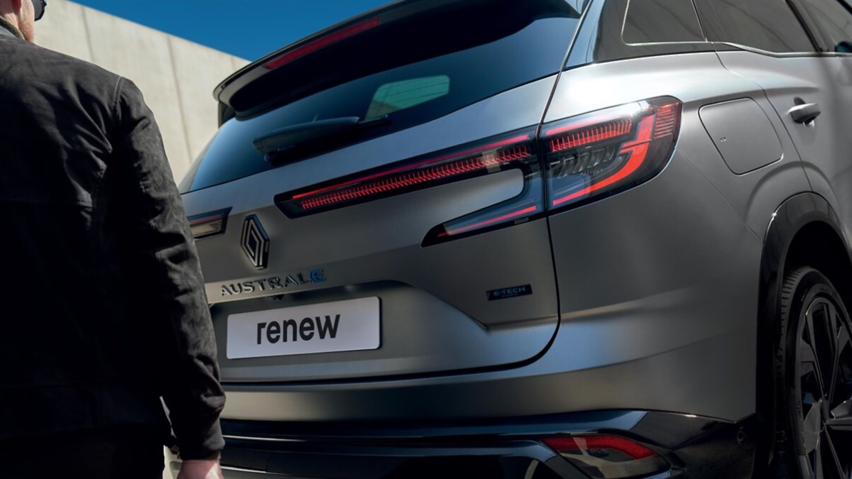 Ženska naslonjena na zadnji del modrega Renault Captur ob sončnem zahodu.
