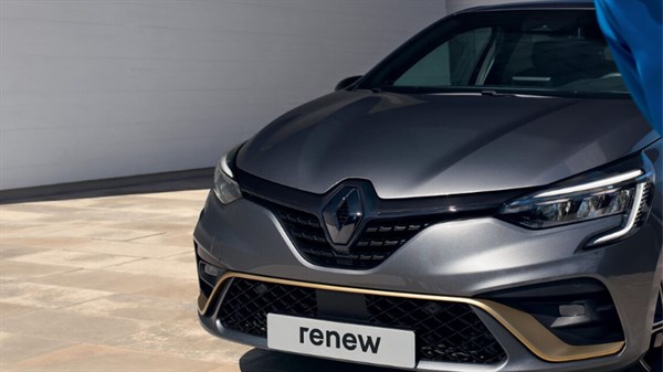 Ženska naslonjena na zadnji del modrega Renault Captur ob sončnem zahodu.
